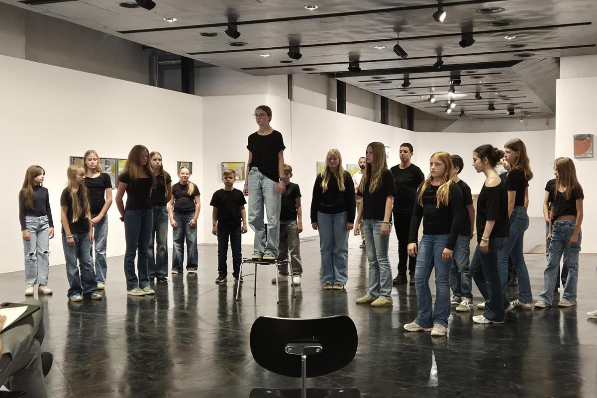 Jugendliche in schwarzen Oberteilen und Jeans stehen in einem Ausstellungsraum vor Kunstwerken.